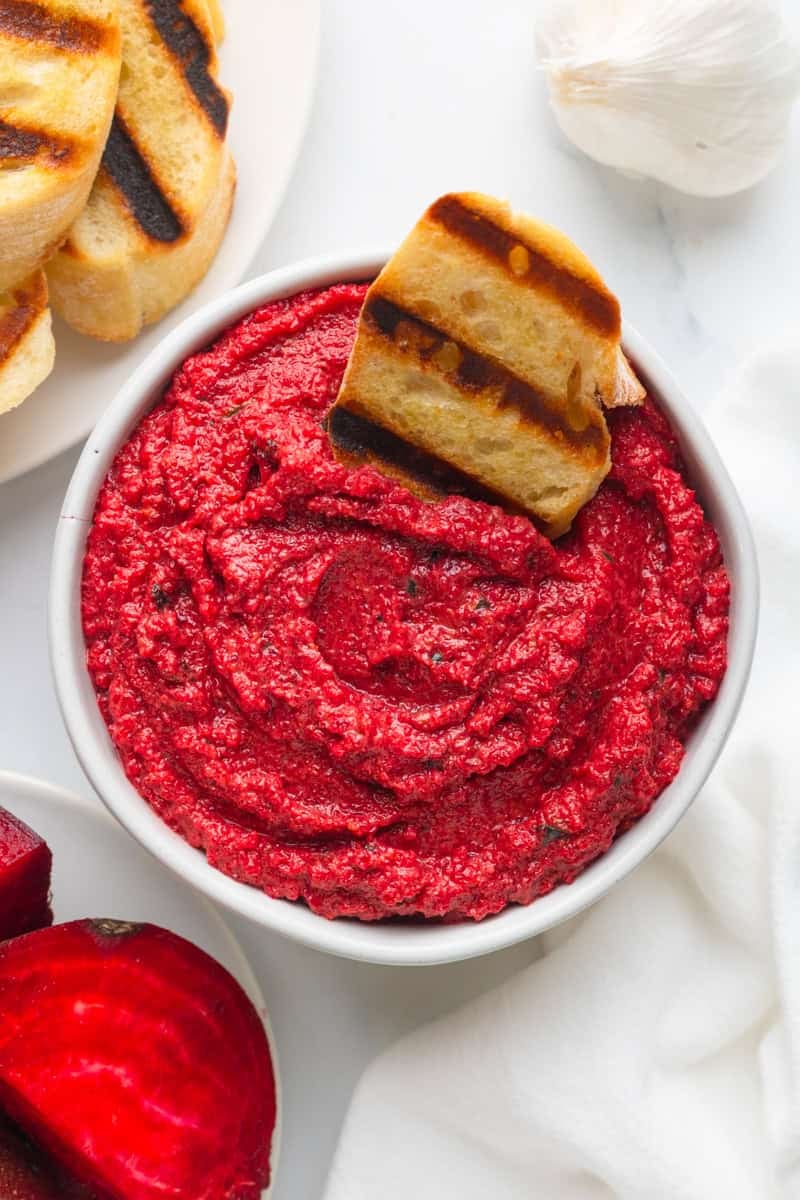 Bowl filled with pink pesto made from beets with a piece of grilled baguette in the pesto.