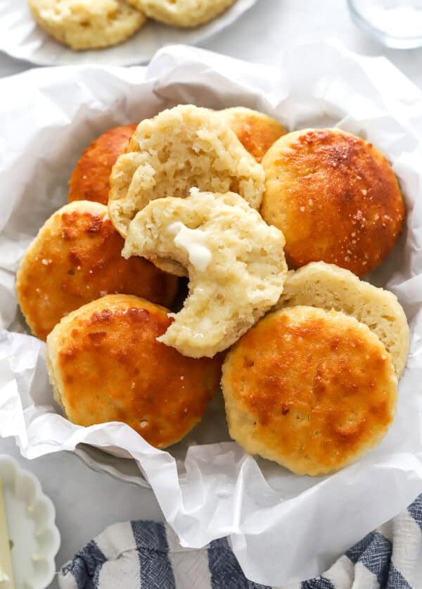 Bowl filled with biscuits made with Greek yogurt with a bite out of one with butter on it.