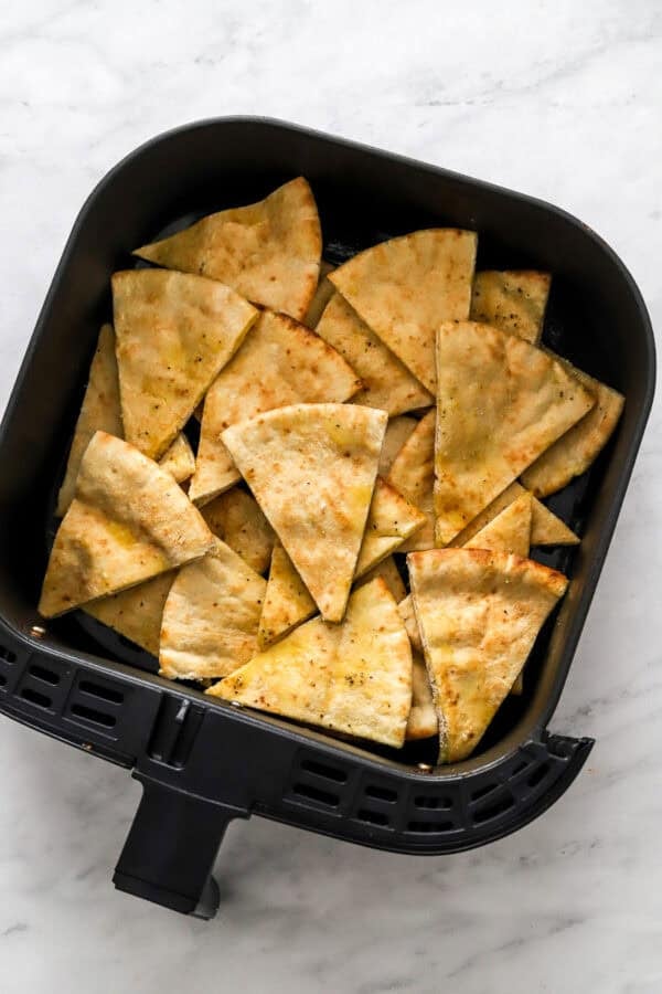 Uncooked pita chips in the air fryer basket.