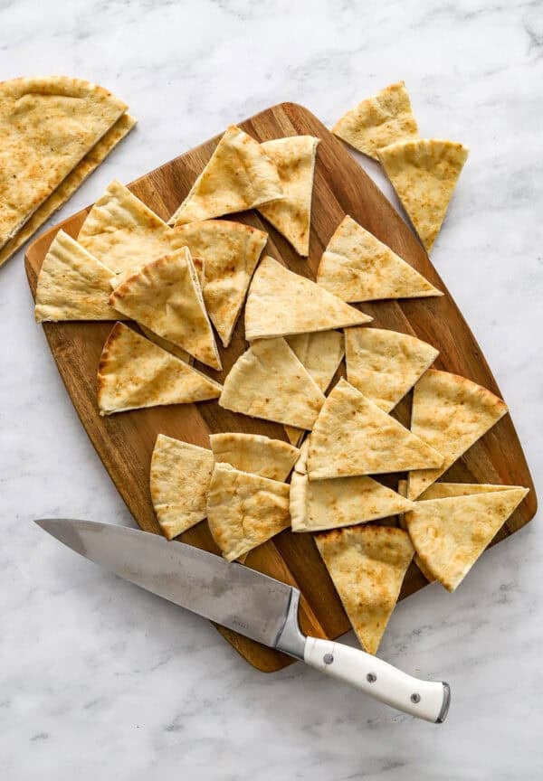 Cut pita pockets on a cutting board with a kitchen knife on the board with it.