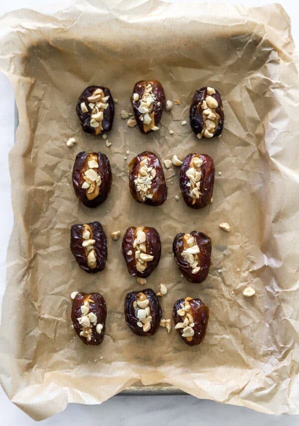 Sliced dates filled with peanut butter and chopped peanuts in rows on a lined baking sheet.