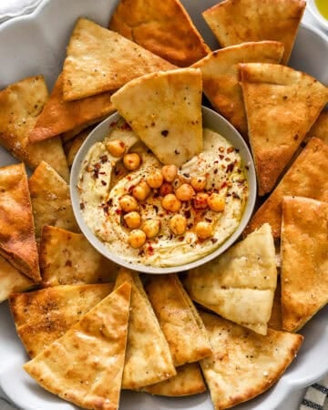 Bowl of hummus on a platter with cooked air fryer pita chips around it.