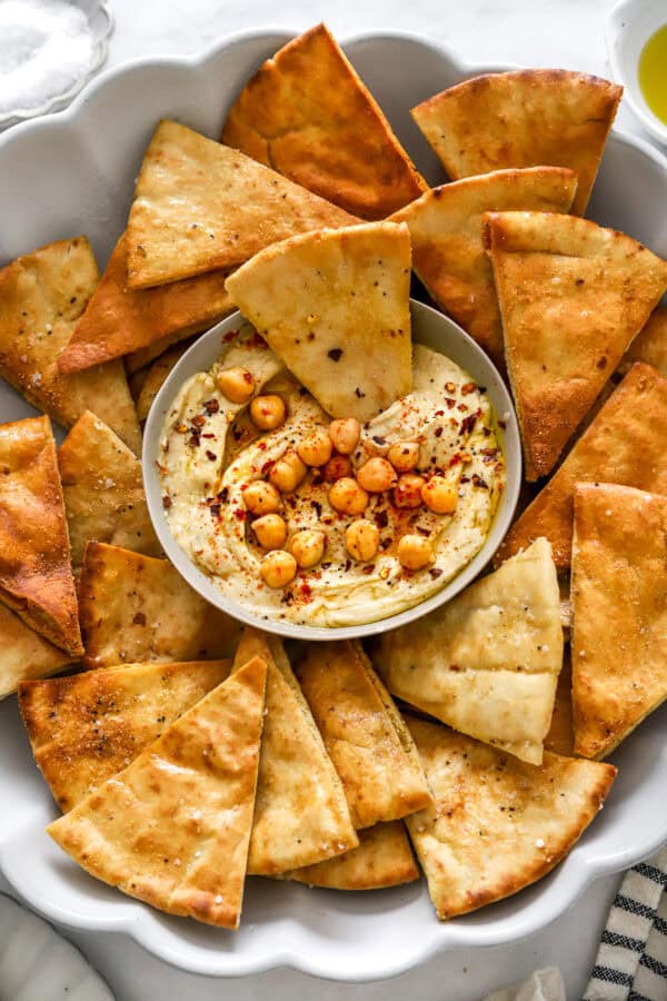 Bowl of hummus on a platter with cooked air fryer pita chips around it.
