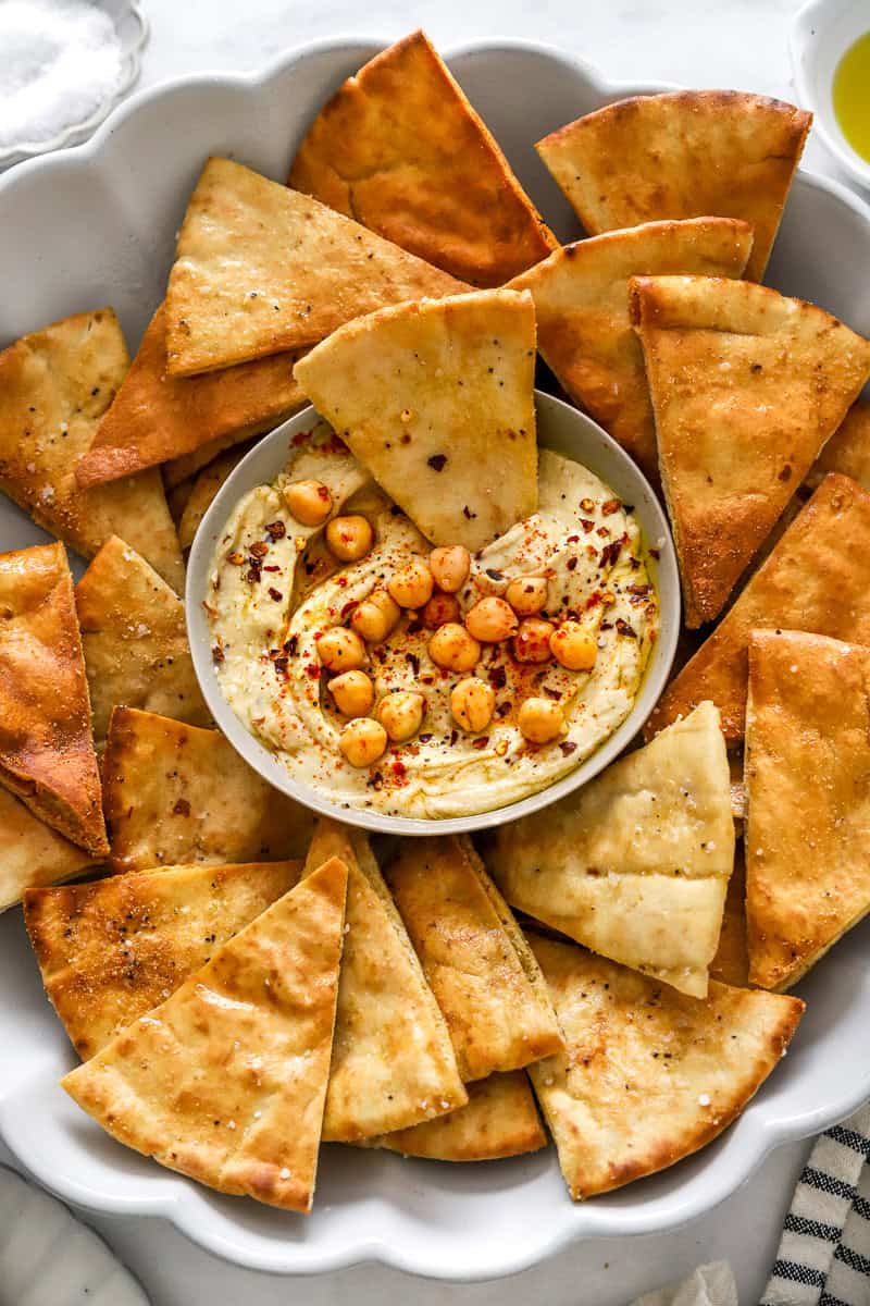 Bowl of hummus on a platter with cooked air fryer pita chips around it.