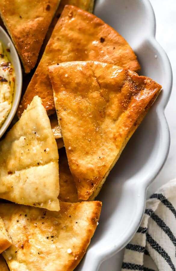 Golden cooked pita chips on a grey platter with a stripped towel next to it.