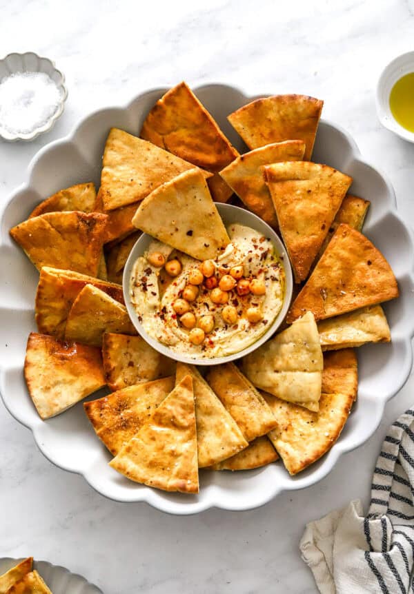 Air fried pita chips on a serving platter with a bowl of hummus in the center of the platter.