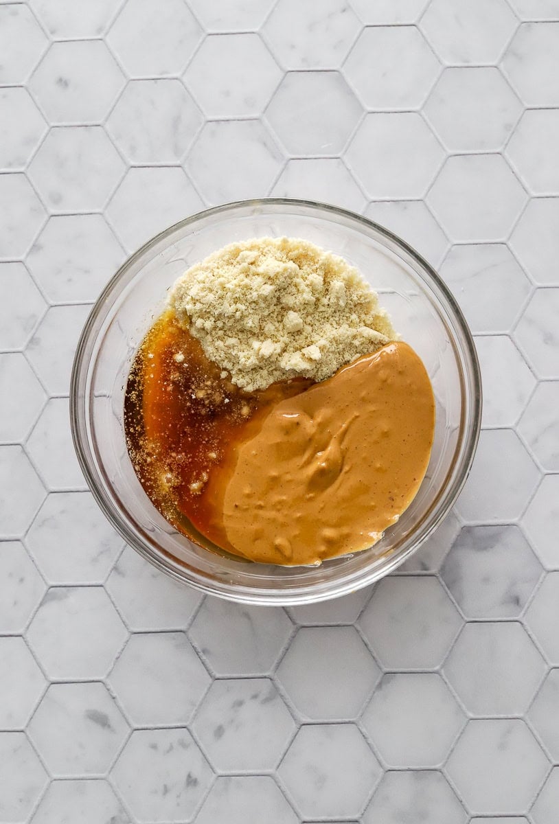 Peanut butter, maple syrup, and almond flour in a glass bowl before being mixed up.
