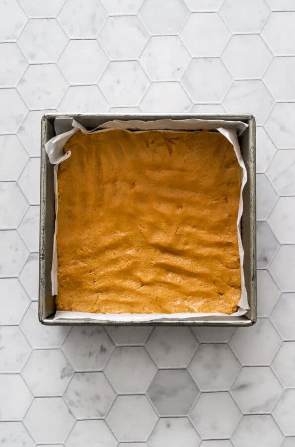 Metal square lined pan with peanut butter bar filling pressed into the bottom of the pan.