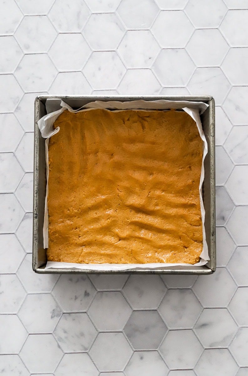 Metal square lined pan with peanut butter bar filling pressed into the bottom of the pan.