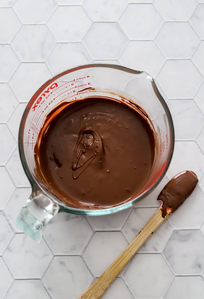 Melted chocolate in a glass measuring cup with a rubber spatula with chocolate on it next to it.
