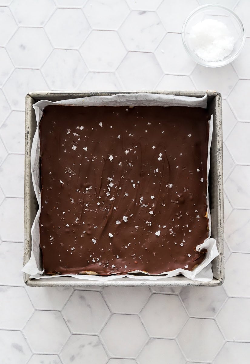 Square metal lined pan with chocolate peanut butter bars with flaky sea salt on top.