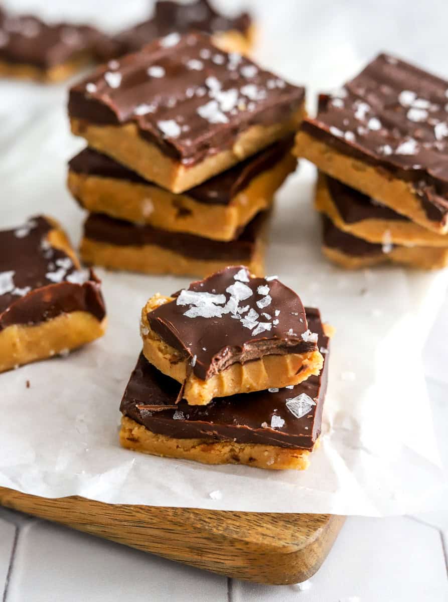 Reeses meant butter bar on top of a cutting board with with parchment paper with one with a bite out of it with stacks of more bars behind it.