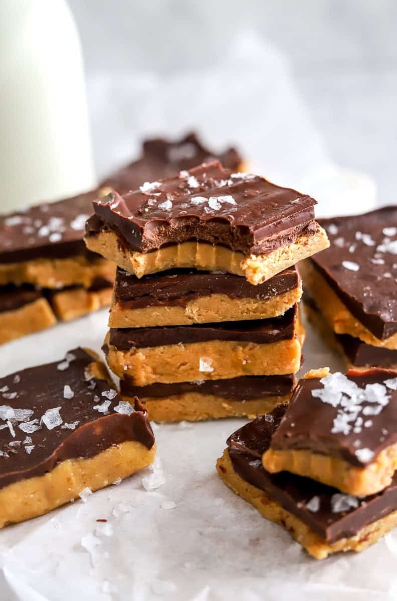 Stack of chocolate pb fudge bars with the top one with a bite out of it with more around it.