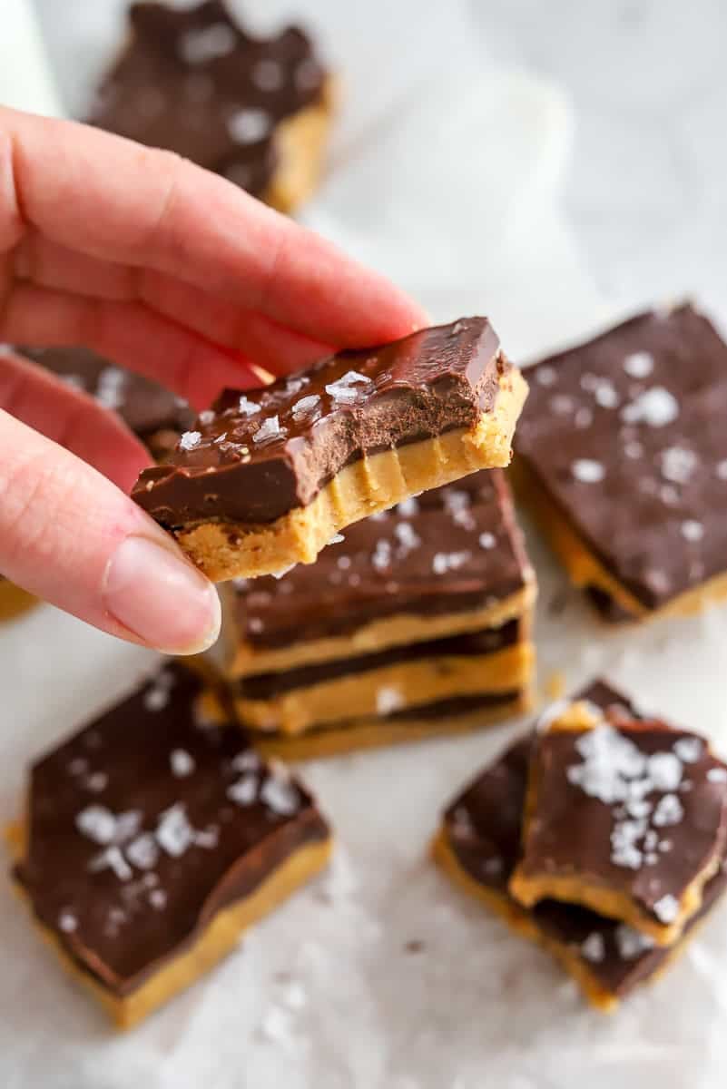 Hand holding chocolate nut butter bar with more behind it.