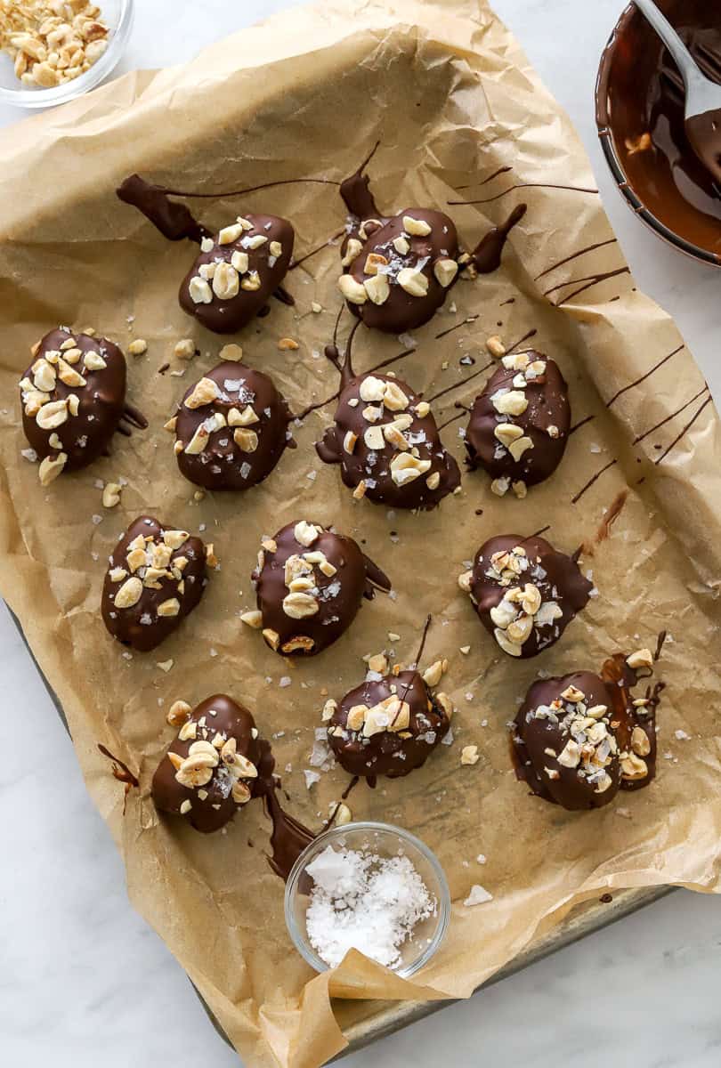 Pan lined with brown paper with date snickers topped with chopped peanuts on them.