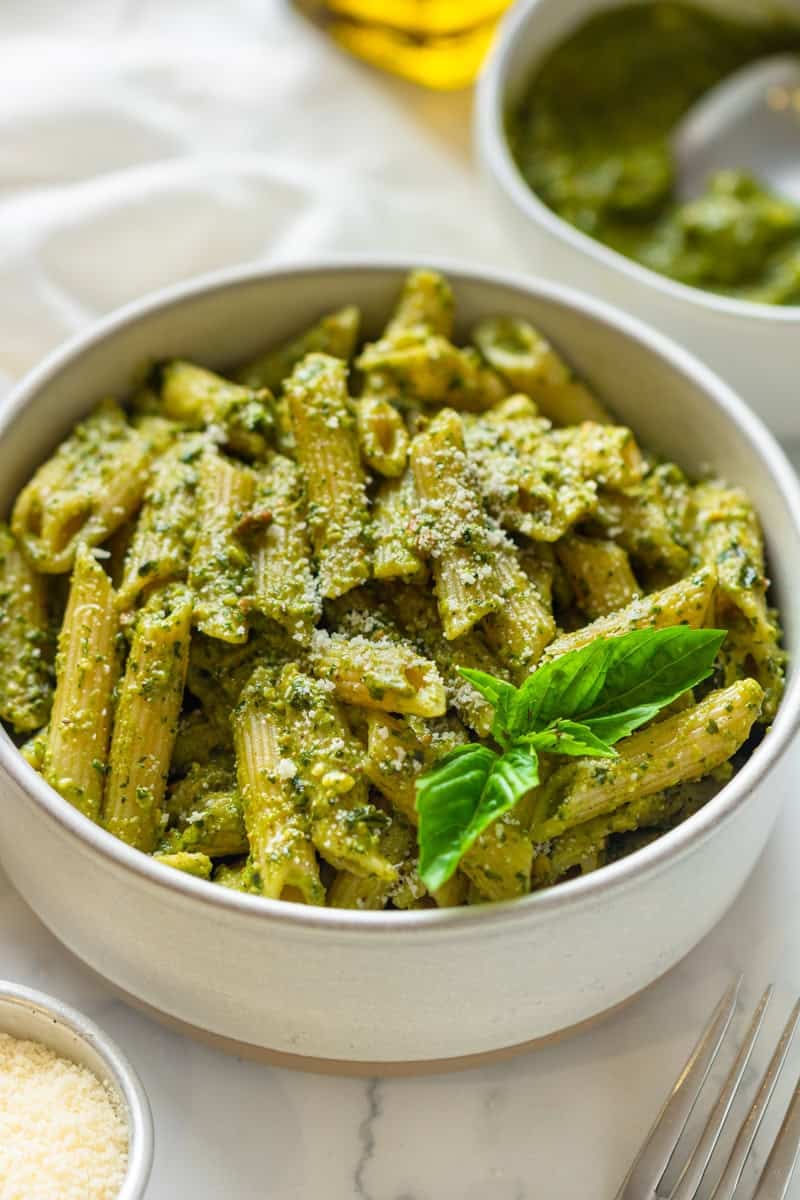 Bowl of penne pasta tossed in homemade basil pesto in a bowl with more pesto in a bowl behind it.