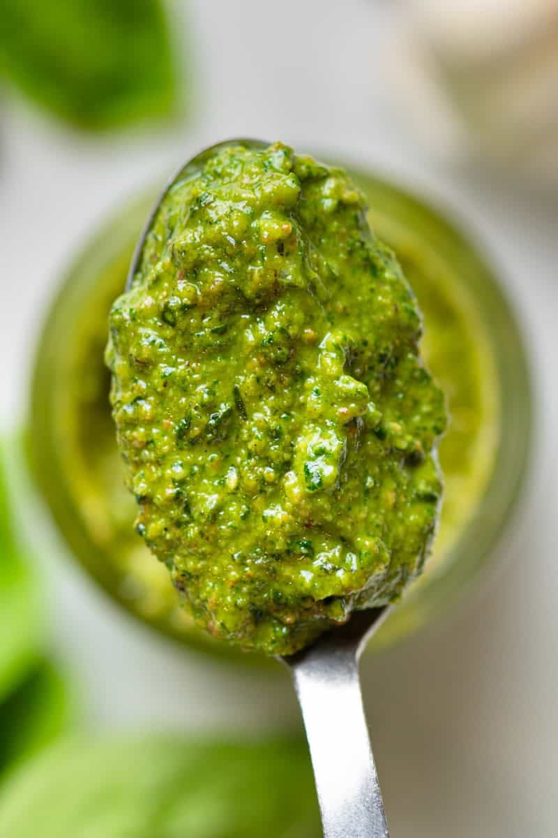 Spoon of basil pesto with more in a bowl behind it.