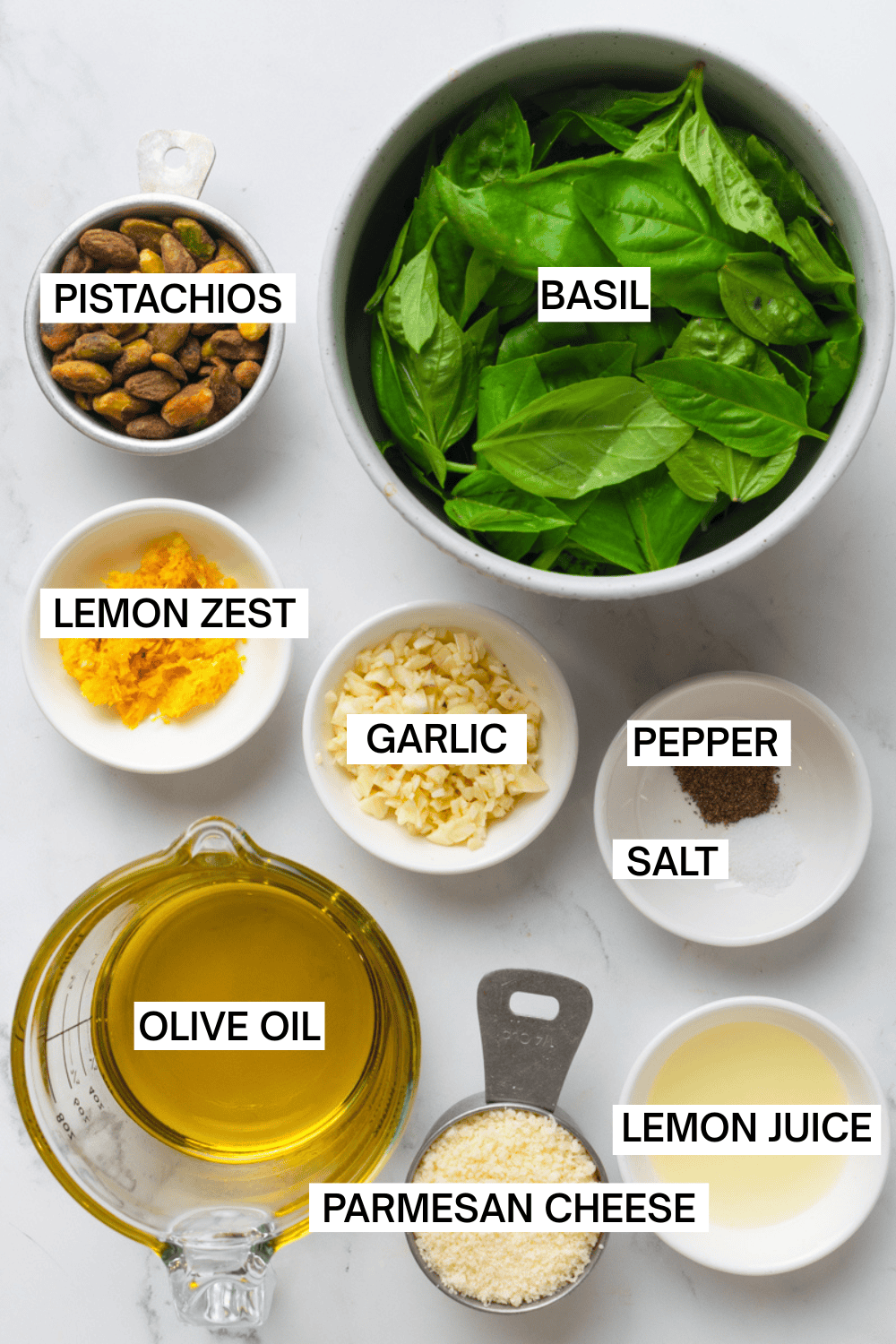 Ingredients for basil pesto in bowls with labels over each ingredient.