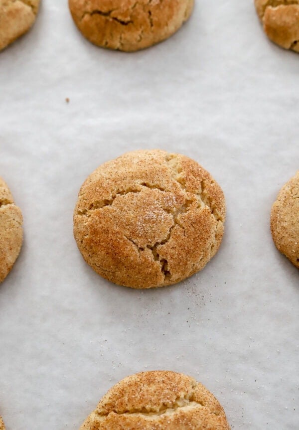 Baked snickerdoodle cookies on a lined baking sheet.