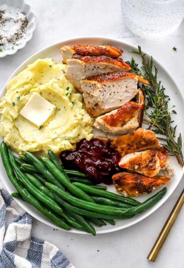 Sliced turkey breast on a plate with mashed potatoes, green beans and cranberry sauce on the plate with it.