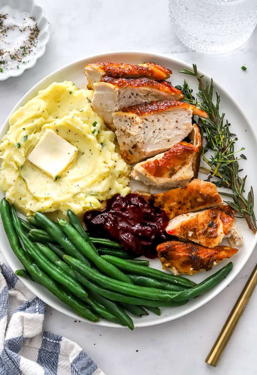 Sliced turkey breast on a plate with mashed potatoes, green beans and cranberry sauce on the plate with it.