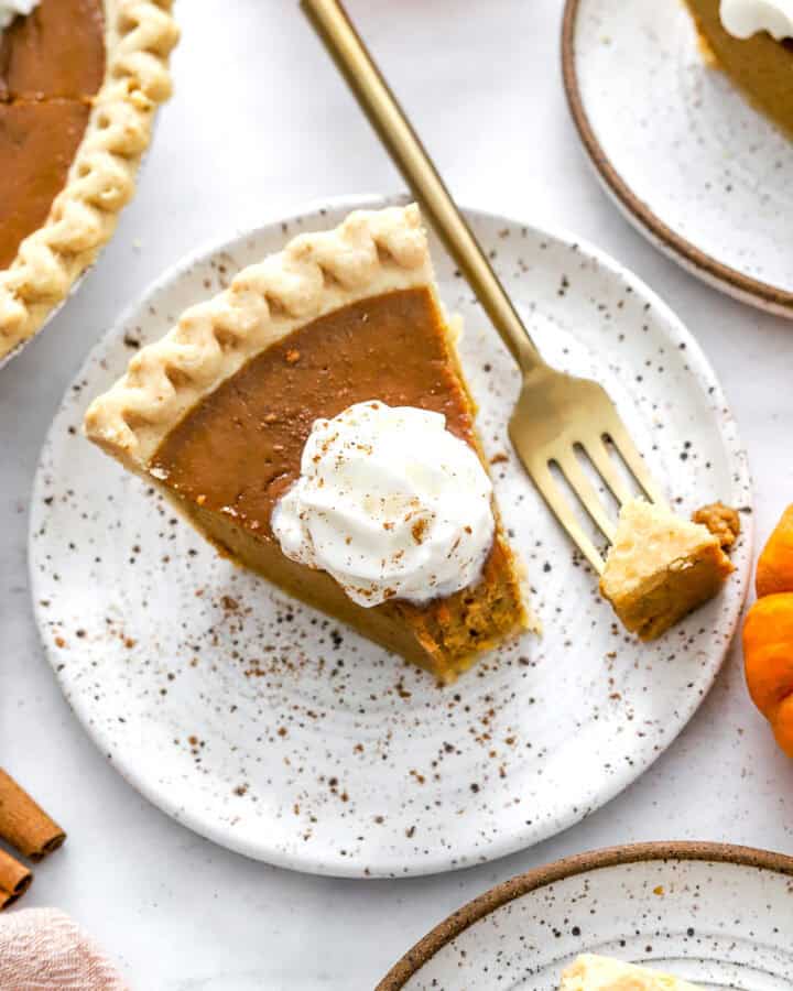 Slice of healthy pumpkin pie on a plate with shipped cream on it.