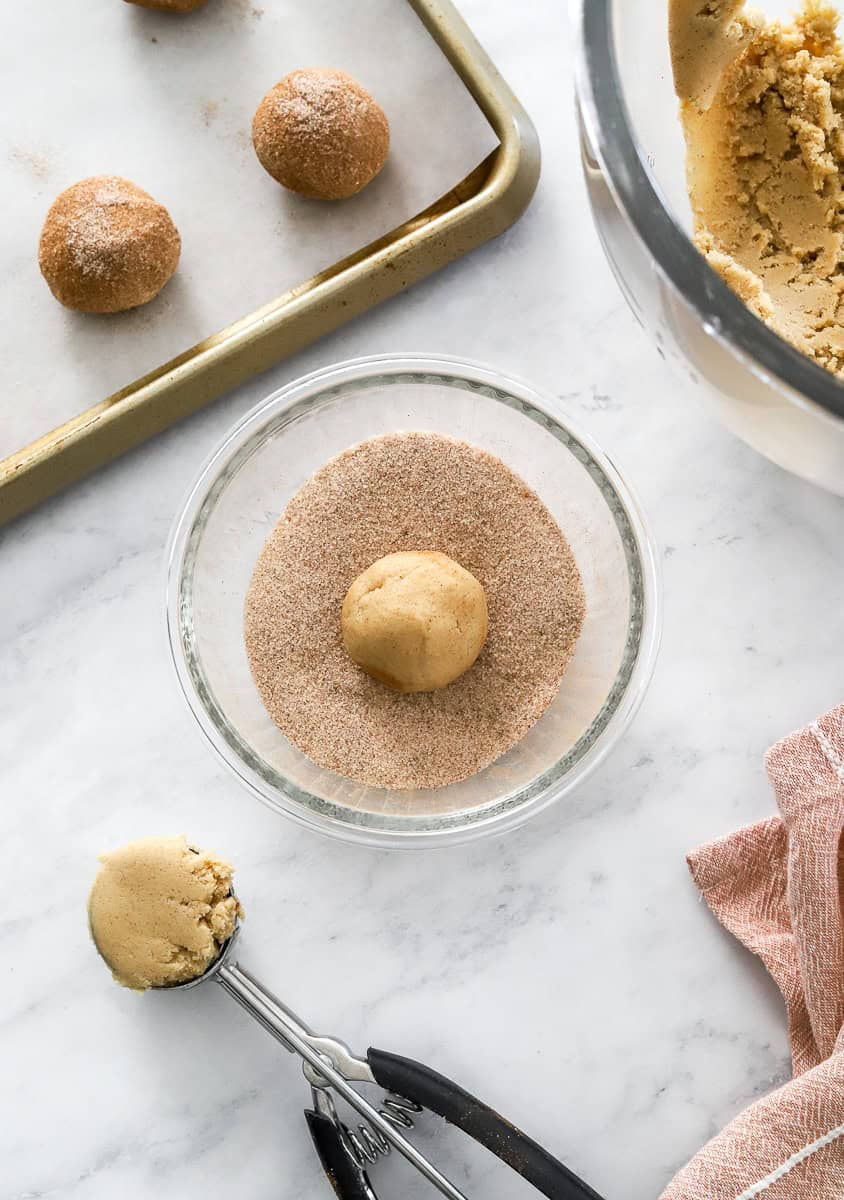 Rolled cookie dough in cinnamon sugar with more behind it.