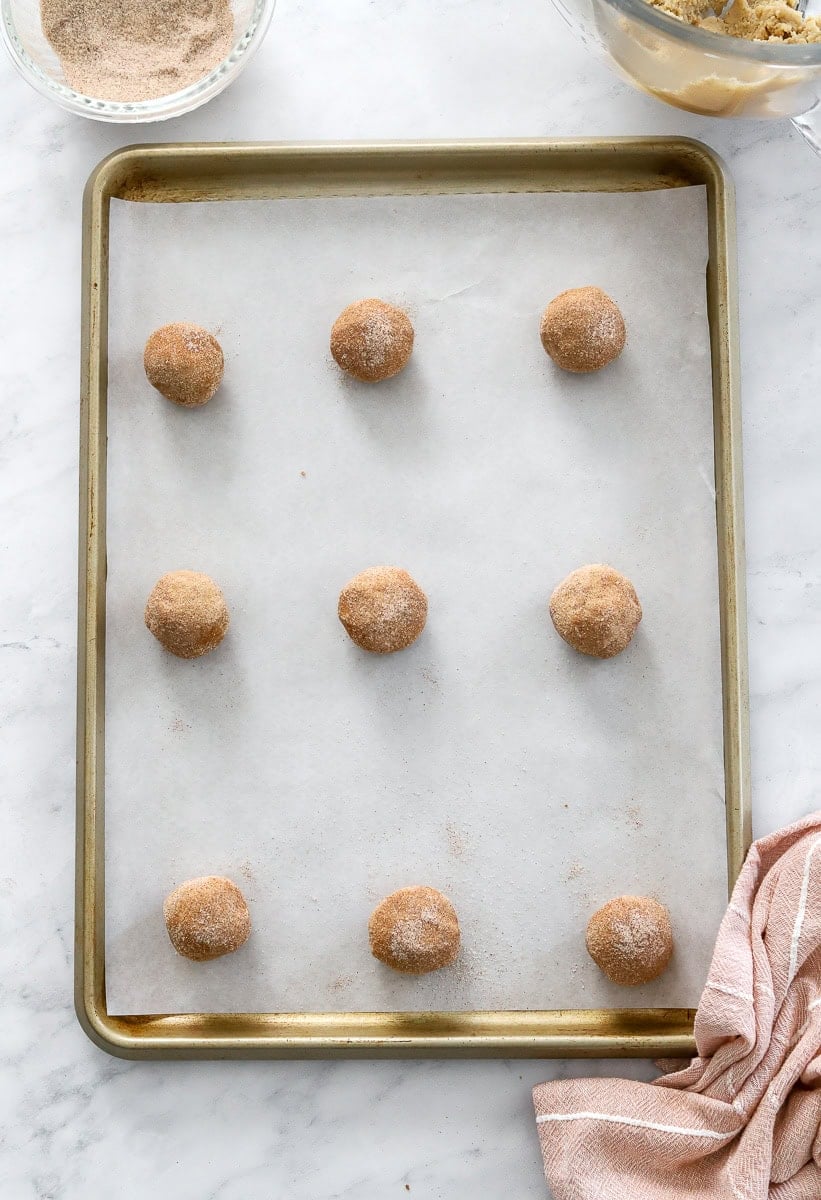 Rolled uncooked snickerdoodle cookie dough balls on a baking sheet.