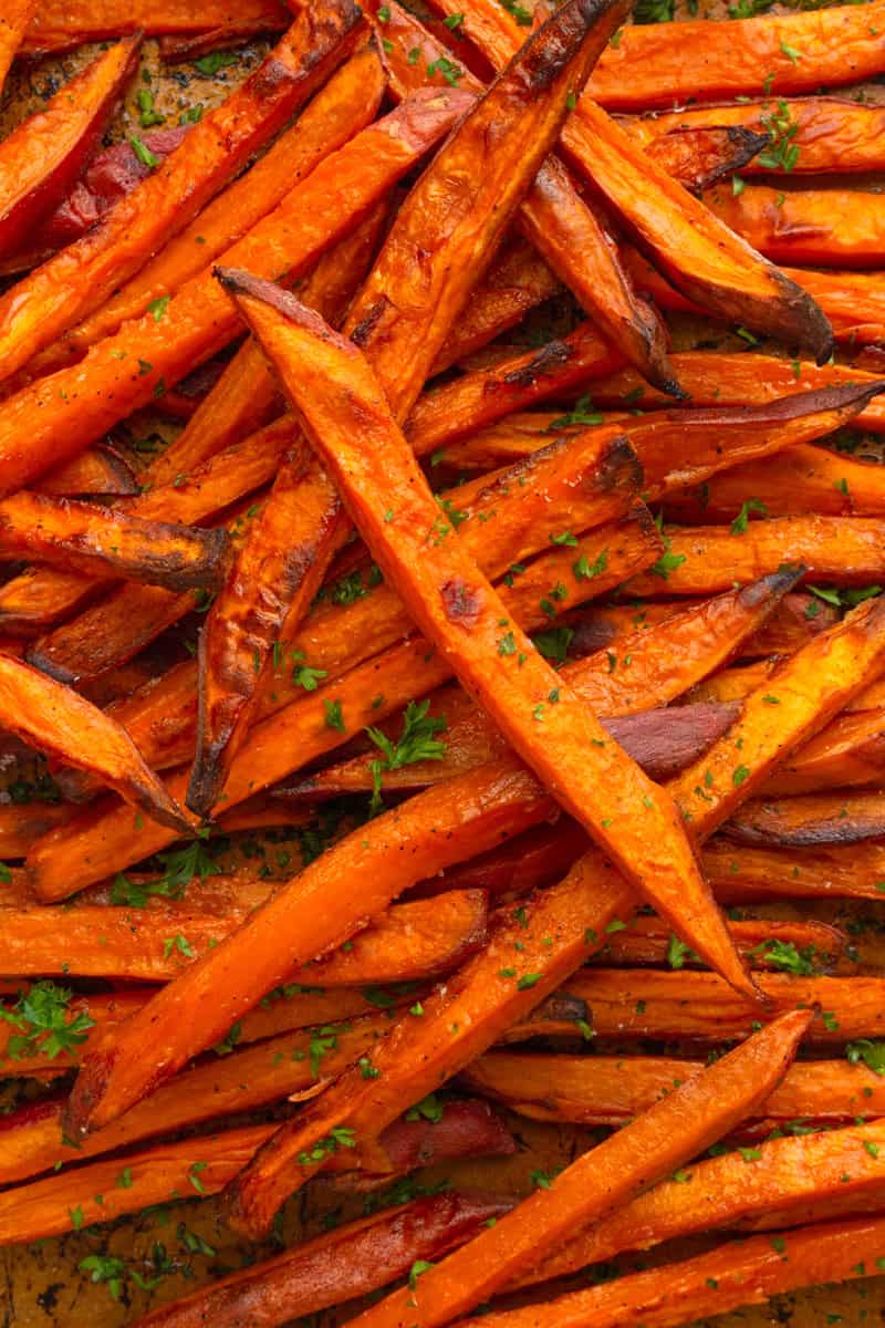 Pile of crispy paleo sweet potato fries with parsley sprinkled on them. 