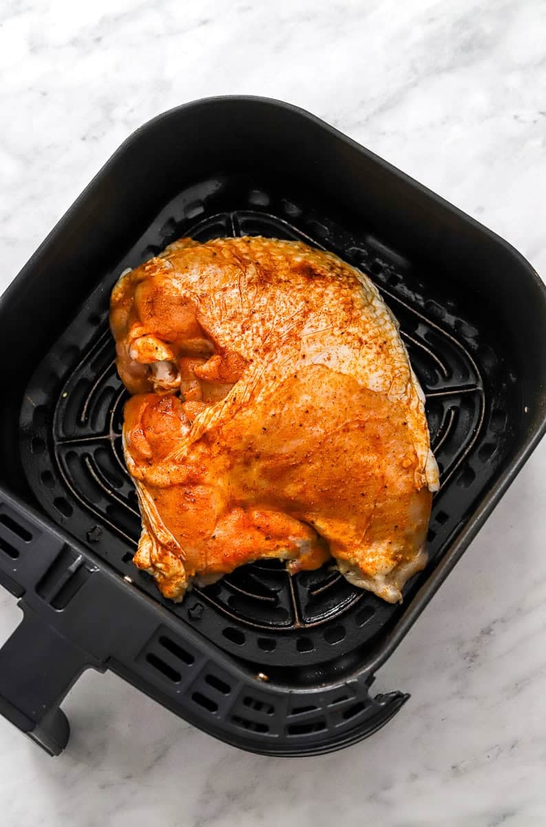 Uncooked turkey breast in the air fryer in black air fryer basket.