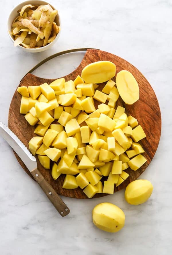 Chopped yellow potatoes on a wood cutting board with a knife on the board.