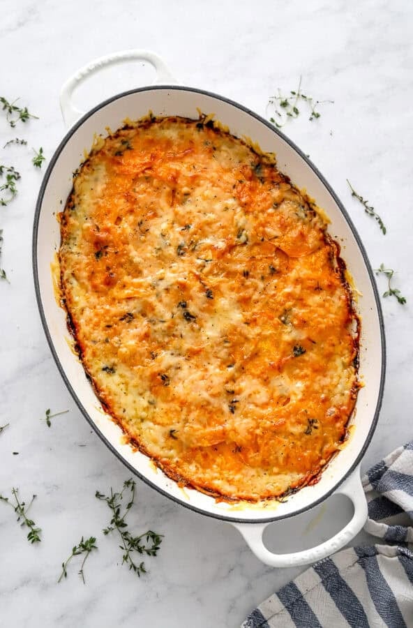 Baked sweet potato grain in a gratin pan with herbs around it.