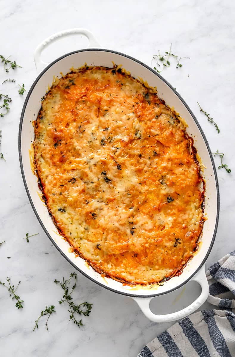 Baked sweet potato grain in a gratin pan with herbs around it.