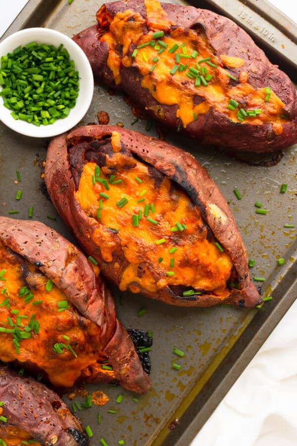 Chili stuffed sweet potatoes on a baking sheet with a bowl of chopped chives on the pan with it.