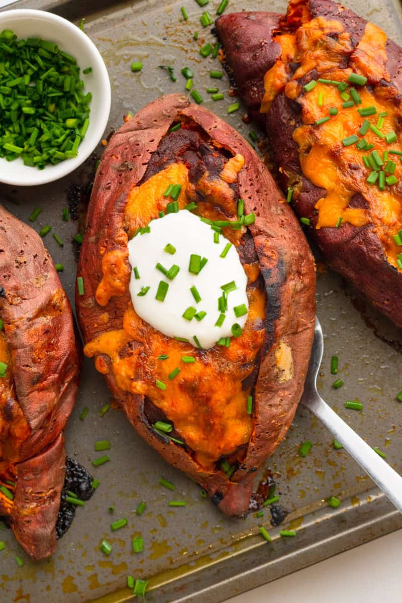 Cooked fill chili sweet potatoes with sour cream and chives on them on a pan. 