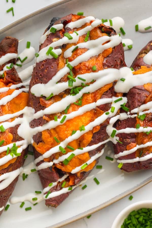Baked filled cheese sweet potatoes with a drizzle of sour cream on them on a white platter.