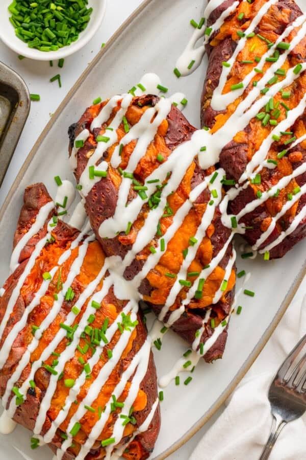 Platter of baked chili filled sweet potatoes with sour cream drizzled on them.