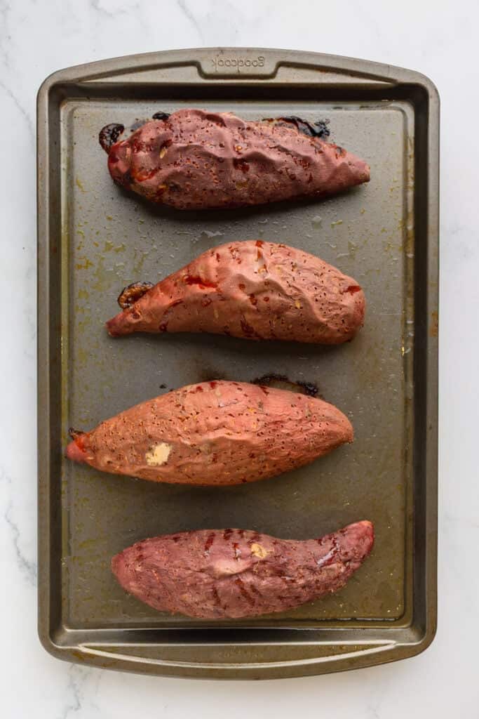 Roasted whole sweet potatoes on a baking sheet. 