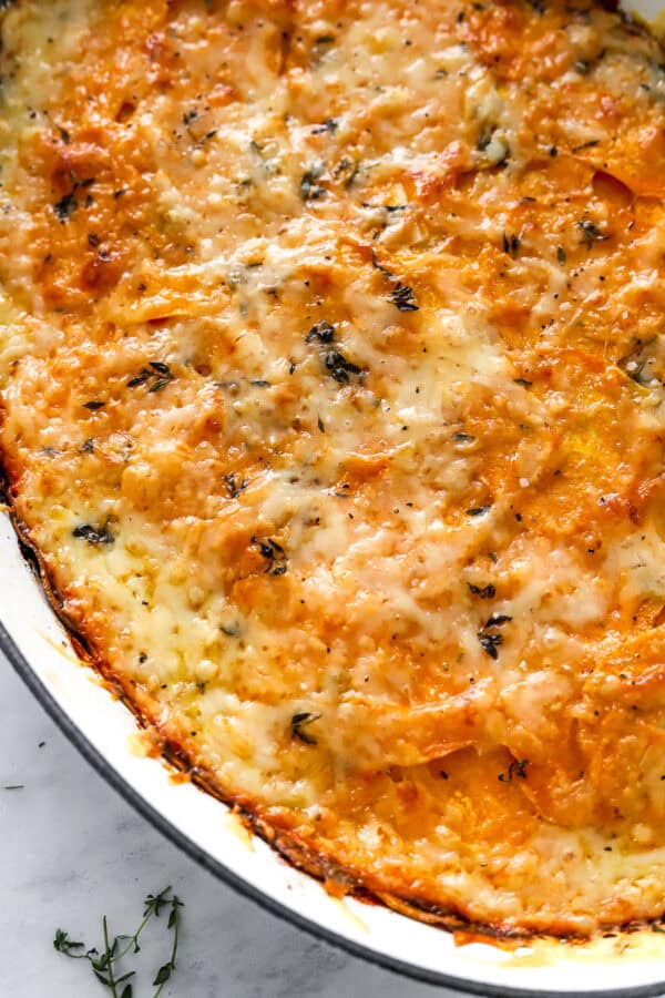 Close up of cheesy gratin sweet potatoes in a white baking dish.
