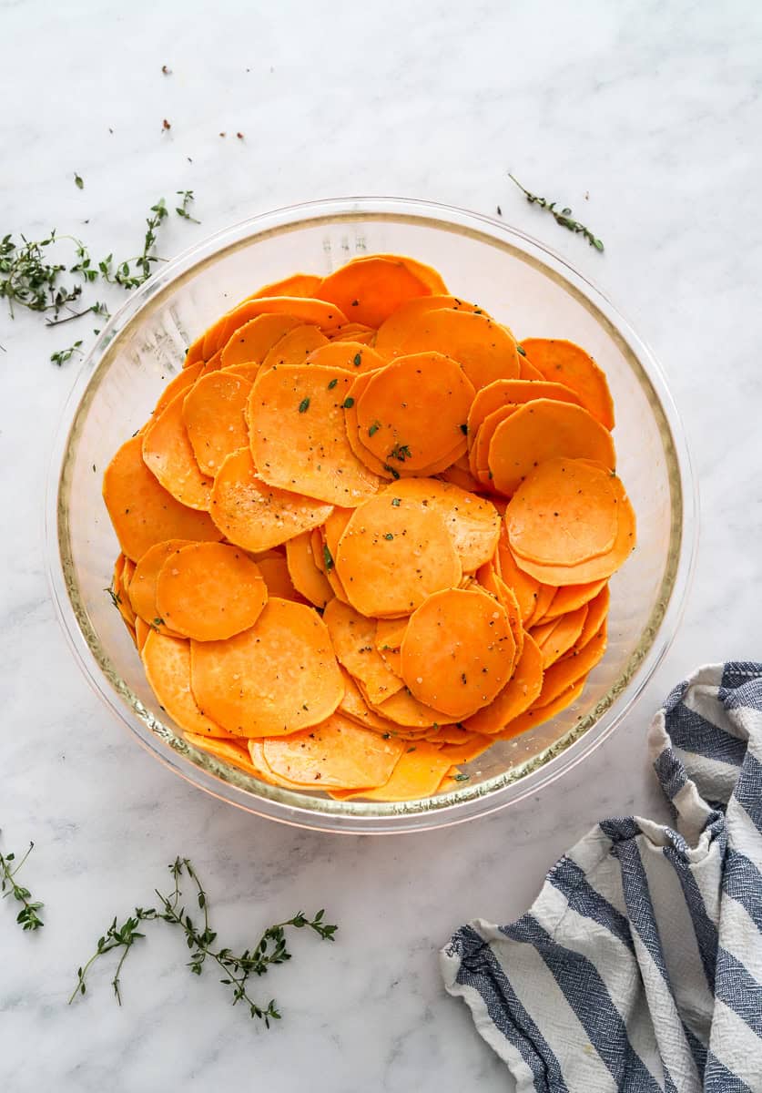 Coated herb sweet potato slices in a bowl with more herbs around it.