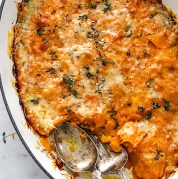 Dish of cheesy gratin with sweet potato with serving spoons in the dish.