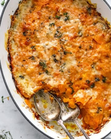 Dish of cheesy gratin with sweet potato with serving spoons in the dish.