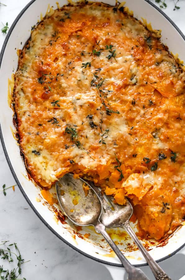 Dish of cheesy gratin with sweet potato with serving spoons in the dish.