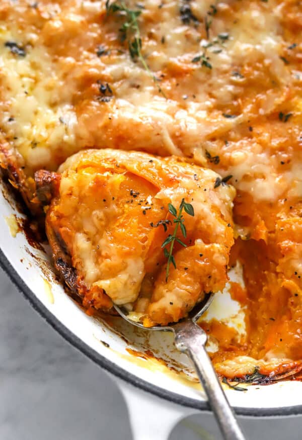 Baking pan filled with sweet potato au gratin with a spoon with some on it in the pan.