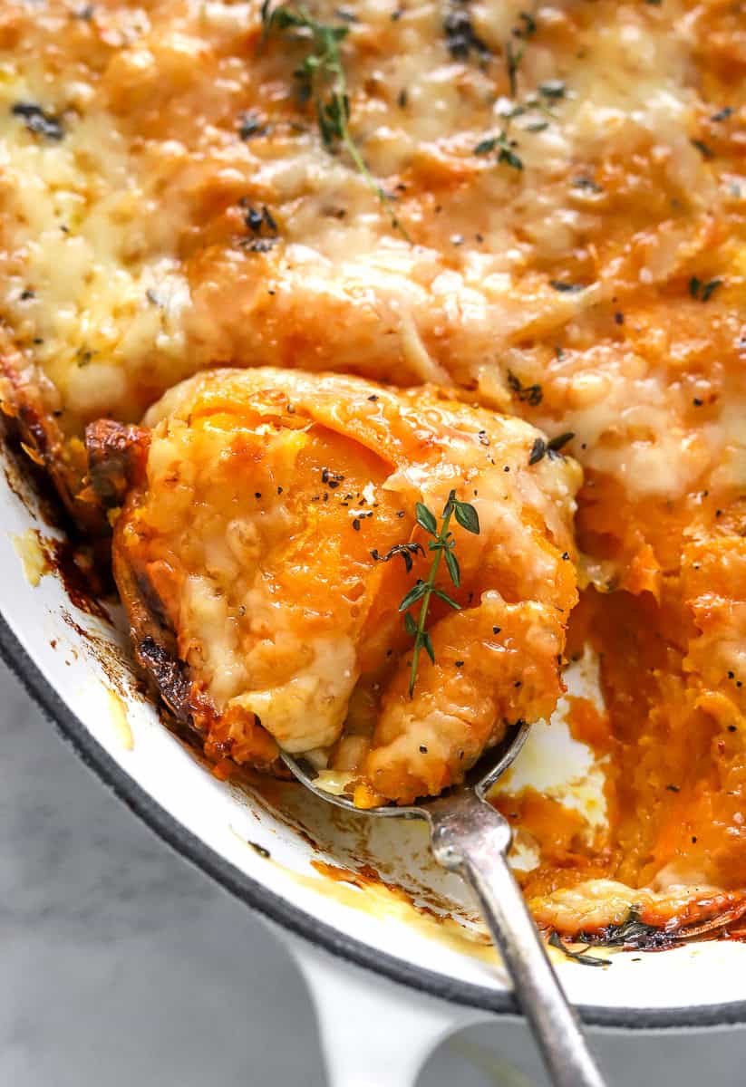 Baking pan filled with sweet potato au gratin with a spoon with some on it in the pan.
