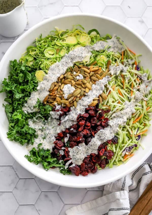 Homemade sweet kale salad kit topped with creamy poppyseed dressing in a white bowl.