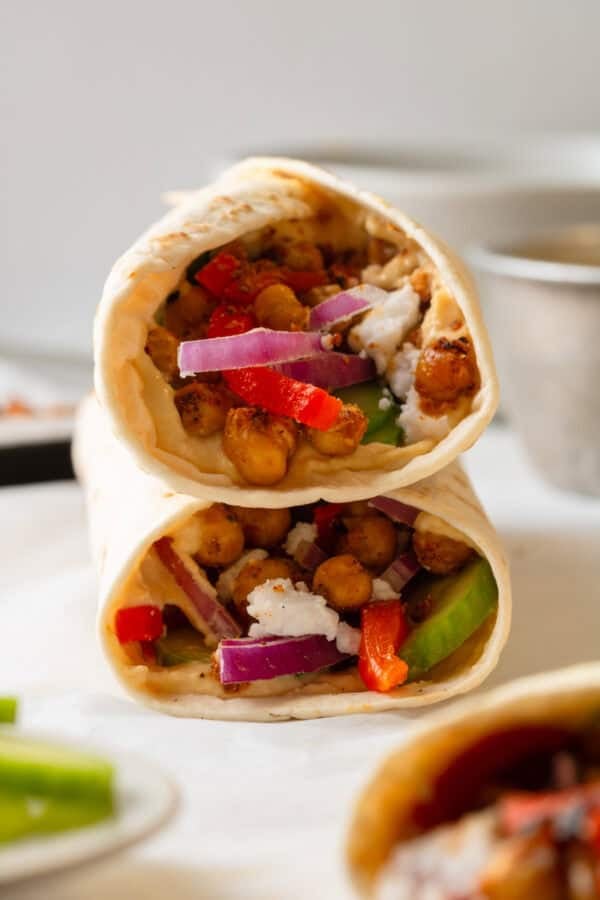 Flour tortilla veggie wrap with hummus stacked on top of one another.