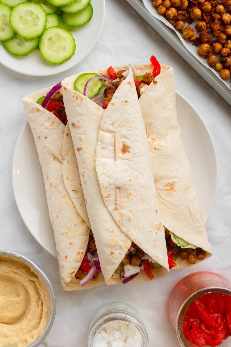 Tortilla hummus wraps on a plate with crispy chickpeas and cucumber in front of it. 