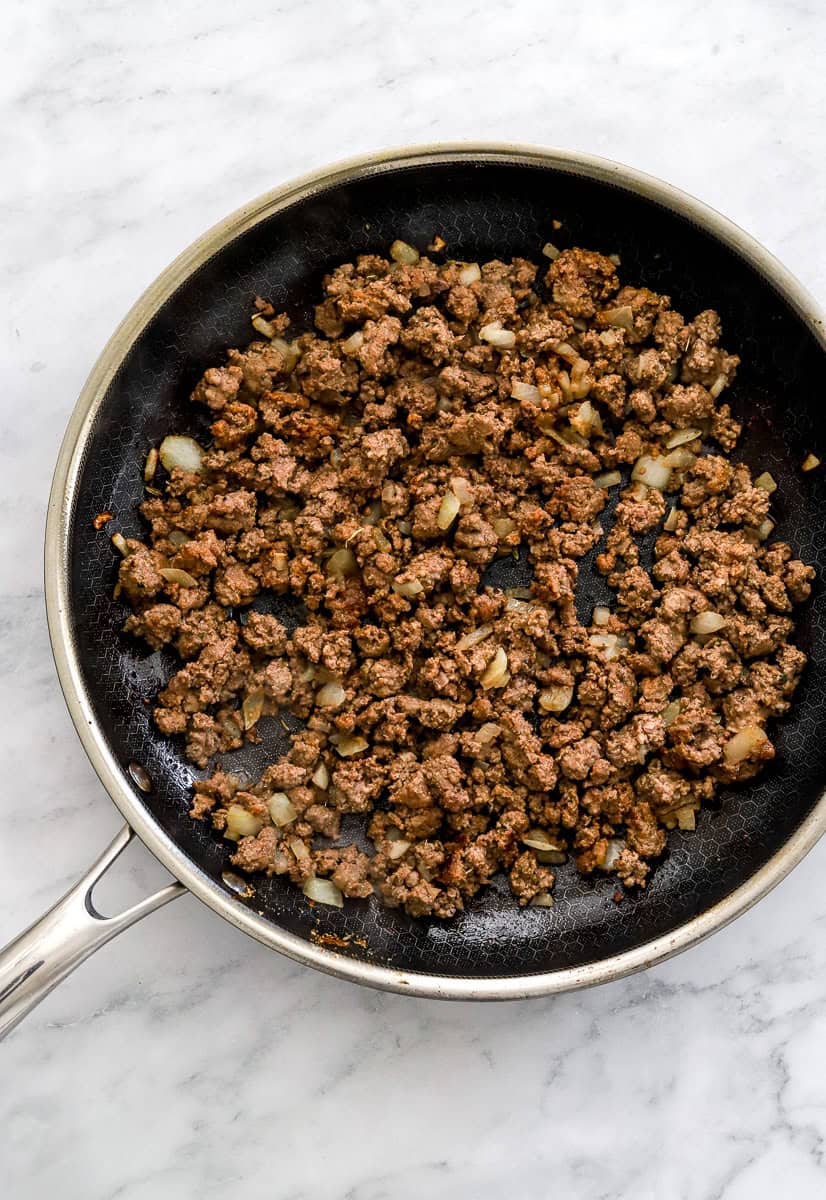 Cooked ground beef and chopped onion in a black sauce pan.