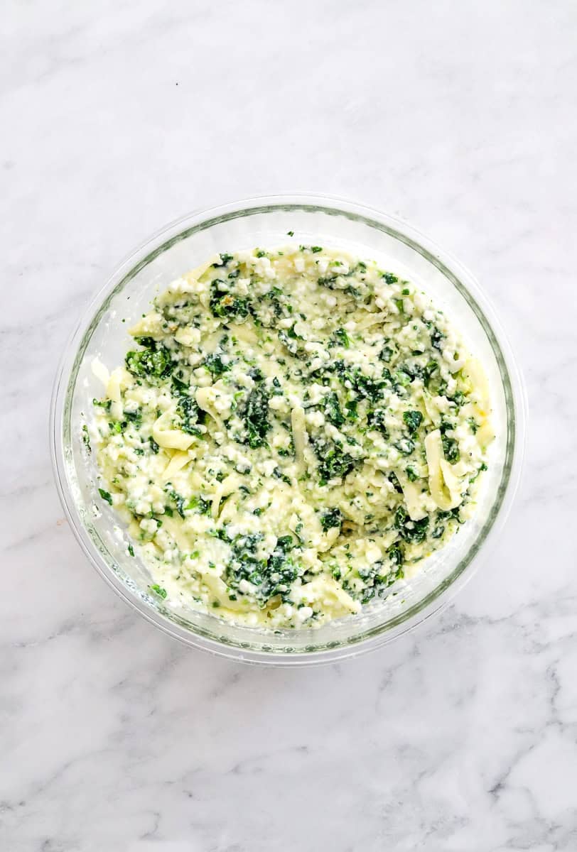 Cottage cheese, egg, parmesan cheese and spinach mixed in a glass bowl.